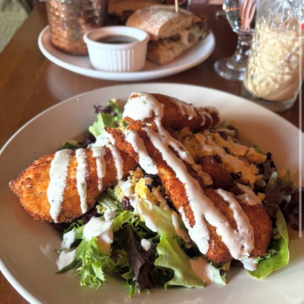 Crispy fried chicken strips with ranch dressing on a fresh green salad at a gastropub.