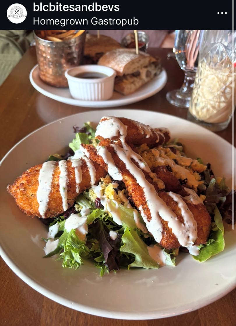 Crispy fried chicken strips with ranch dressing on a fresh green salad at a gastropub.