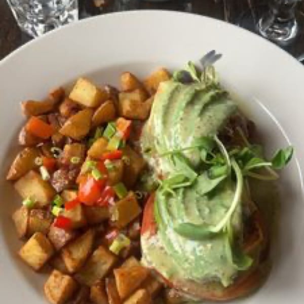 Vegan Benedict with avocado and microgreens, served with crispy roasted potatoes and chopped vegetables.