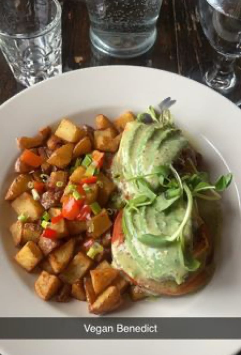 Vegan Benedict with avocado and microgreens, served with crispy roasted potatoes and chopped vegetables.
