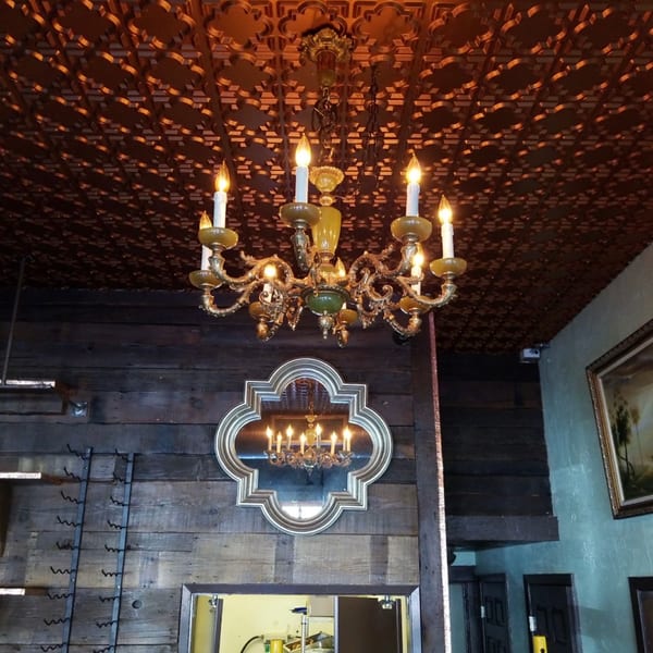 Golden chandelier illuminates a patterned ceiling and wooden wall with a decorative mirror.