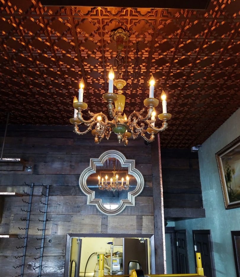 Golden chandelier illuminates a patterned ceiling and wooden wall with a decorative mirror.