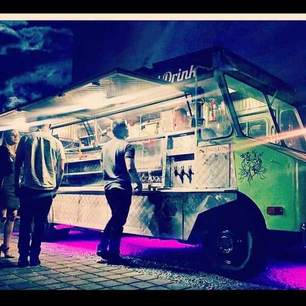 Green food truck at night with people ordering, illuminated by purple underglow.