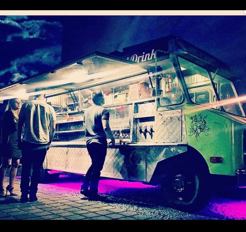 Green food truck at night with people ordering, illuminated by purple underglow.