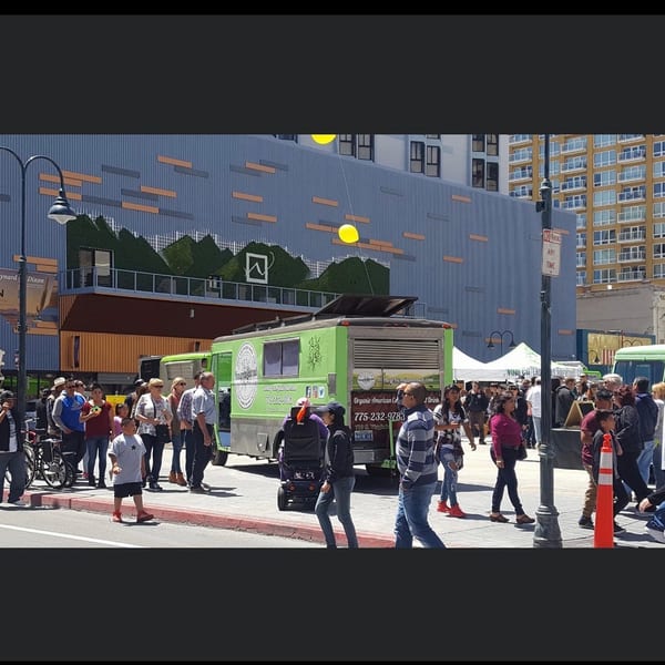 Organic American Co food truck serving customers on a busy city street with buildings and a mural.