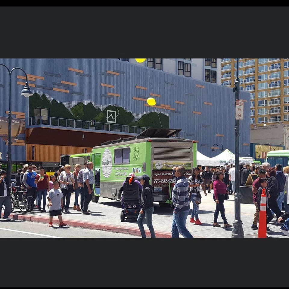 Organic American Co food truck serving customers on a busy city street with buildings and a mural.