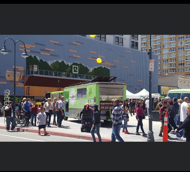 Organic American Co food truck serving customers on a busy city street with buildings and a mural.